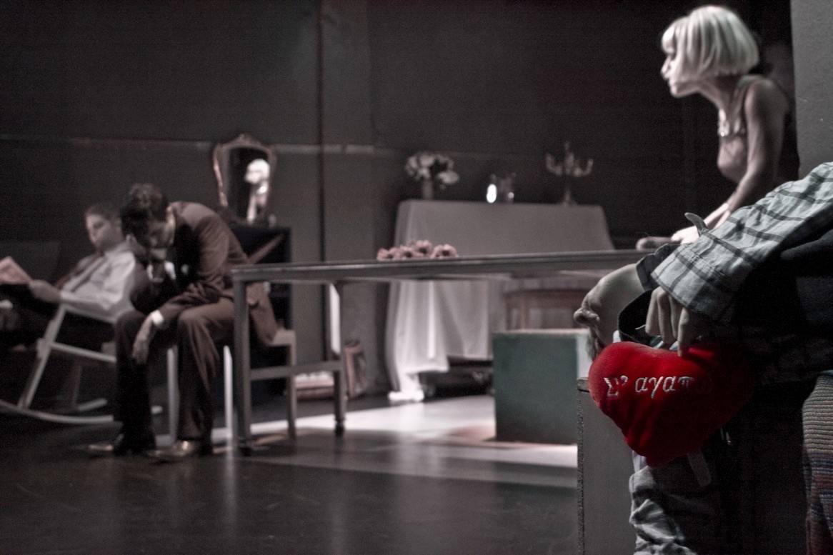 Δύο άντρες και μια γυναίκα κάθονται, ένα χέρι κρατάει μια καρδιά που γράφει «Σ' αγαπώ»