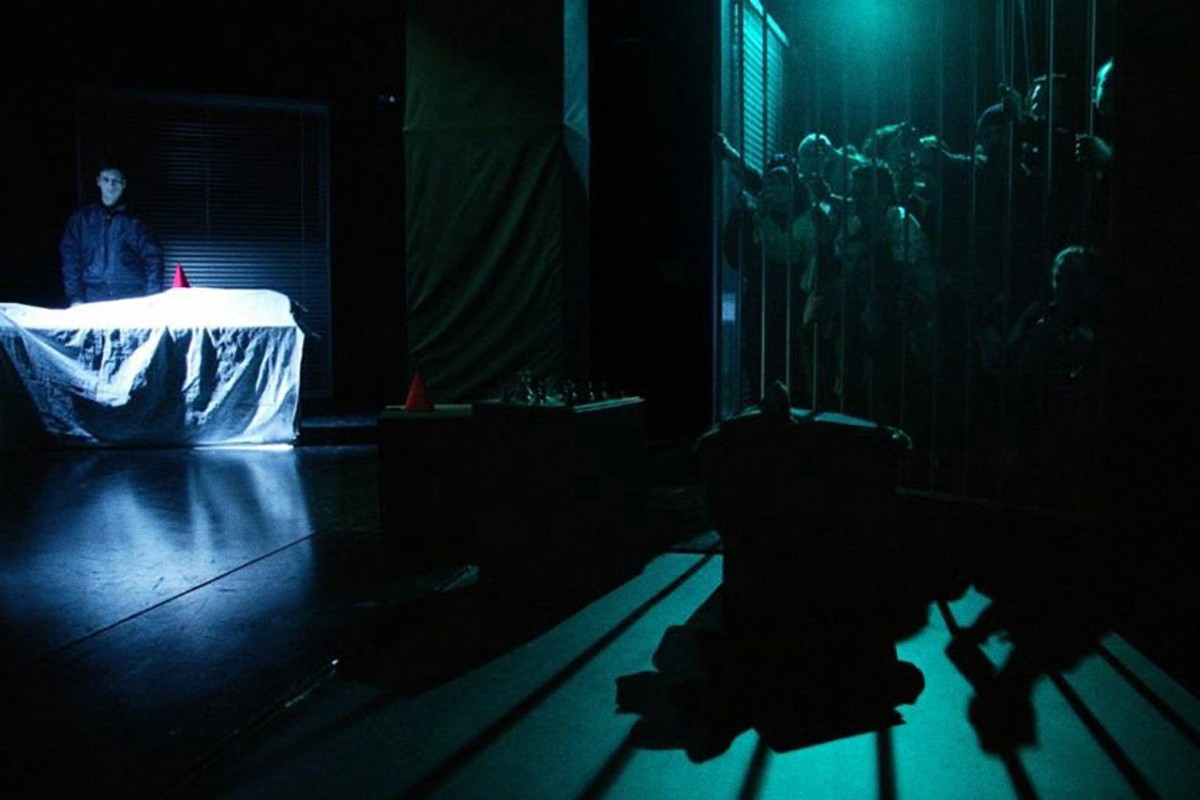 Αρκετοί σπουδαστές πίσω απο κάγκελα. Ένας άντρας στέκεται πίσω από ένα τραπέζι καλυμμένο με σεντόνι